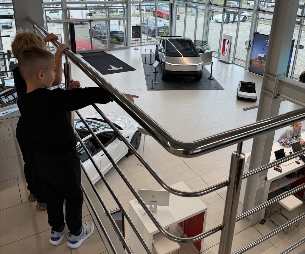 Dzieci obserwujące z antresoli salon Tesla Center Warsaw z Cybertruckiem i jego miniaturową wersją